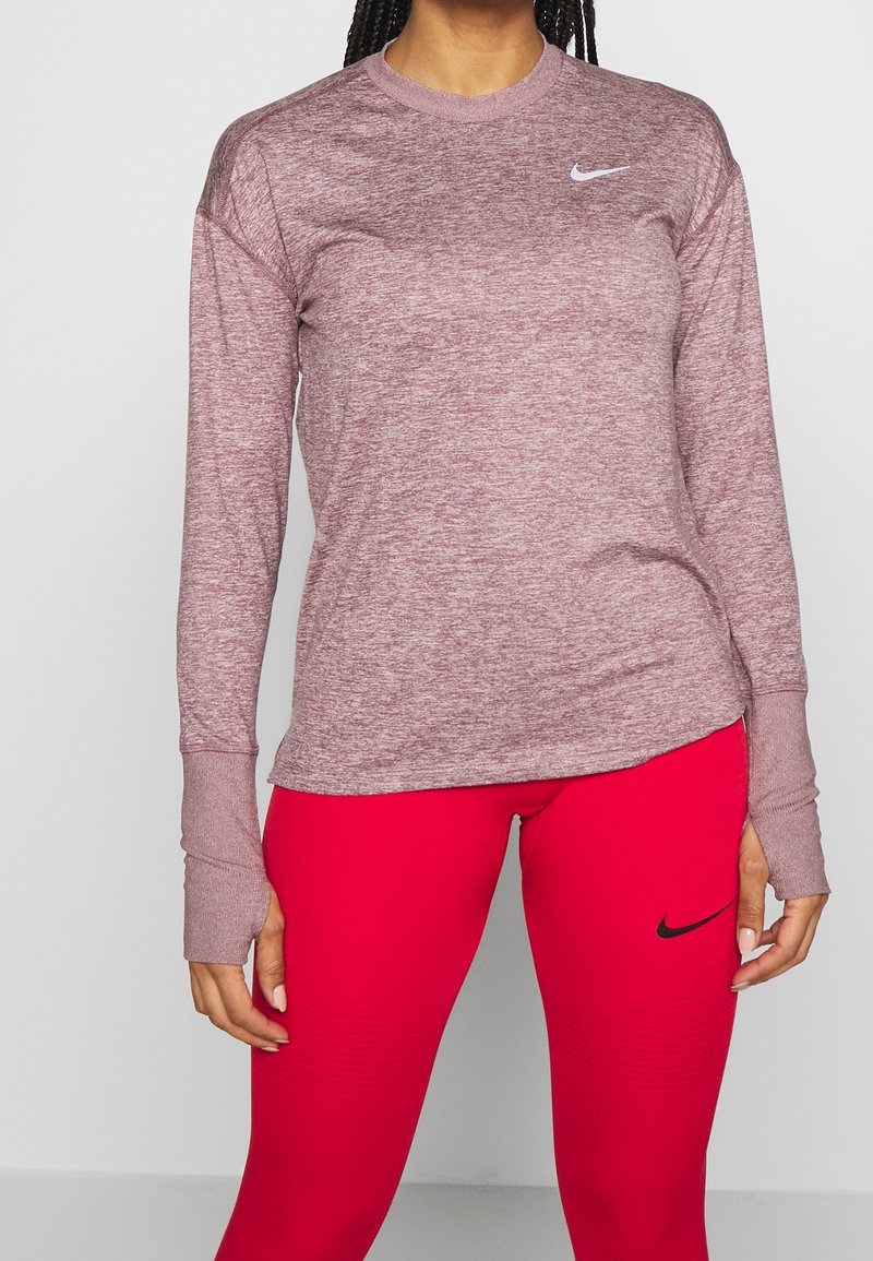 Maglia sportiva bordeaux a maniche lunghe con scollo tondo e fori per il pollice, abbinata a leggings rossi con logo Nike Swoosh nero.