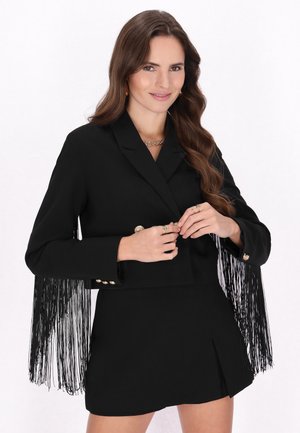 Musta bleiseri, jossa on fringed yksityiskohtia hihoissa, kultaiset nappikoristeet ja lyhyt leikkaus. Suora pinta, yhdistettynä sopivaan mustaan mini-hameeseen.