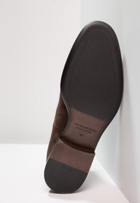 Suela de bota de ante marrón con fondo de goma negra. Presenta un tacón curvado y un logo en relieve. Talla 42 indicada. Textura limpia y suave.