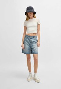 Valkoinen ribbed crop top, vaaleansiniset farkkushortsit ja tummansininen bucket-hattu. Paksut valkoiset lenkkarit, joissa on tekstuuripohjat. Yksinkertainen ja rento muotoilu.