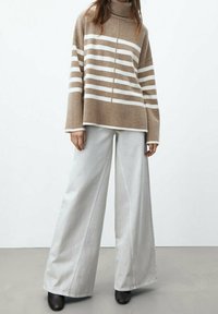 Beżowy i biały sweter w prążki z golfem, w połączeniu z szerokimi, jasnoszarymi spodniami. Czarne botki do kostek dopełniają stylizację.