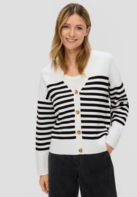 Schwarz-weißer gestreifter Cardigan mit V-Ausschnitt, fünf großen Knöpfen, gerippten Bündchen und lockerer Passform, kombiniert mit dunklen Jeans.