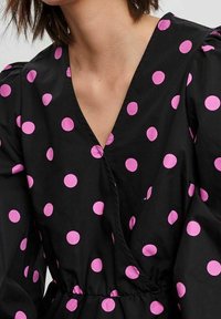Vestito nero con grandi pois rosa, scollatura a V e maniche a sbuffo; realizzato in un tessuto morbido con vita arricciata.