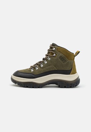 Grüne Wildleder-High-Top-Stiefel mit schwarzer Gummisohle, runder Zehenpartie, Metallösen und khakifarbenen Akzenten. Mit einer Zuglasche an der Ferse.
