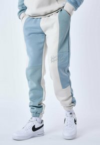 Pantalones de chándal con un diseño de bloques de color que presenta paneles en azul y crema; cinturilla y puños elásticos, detalle bordado en el costado.