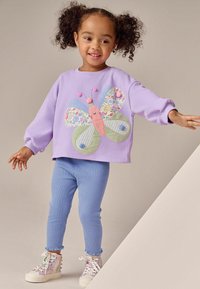 Bluza mov cu design de fluture care include modele florale, dungi și uni. Asortată cu colanți bleu deschis cu textură și adidași cu model.