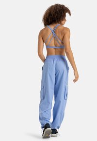 Camiseta deportiva sin mangas azul claro con diseño de tirantes cruzados, combinada con pantalones cargo azul claro con bolsillos laterales y puños elásticos.