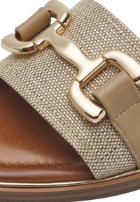 Sandalo con cinturino intrecciato beige e dettaglio in pelle marrone, accentuato da una fibbia dorata. Sole piatto con una leggera lucentezza.