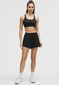 Sostenedor deportivo negro y pantalones cortos negros, hechos de una tela suave. Los pantalones cortos tienen una cinturilla elástica con un cordón. Zapatillas deportivas blancas.