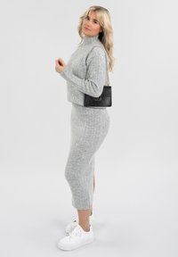 Ensemble en tricot à côtes gris composé d'un haut à col montant et d'une jupe jusqu'aux genoux, associé à un sac à main noir texturé et des baskets blanches.