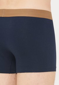 Boxershorts aus einem navyblauen Baumwollmix mit glatter Textur, ausgestattet mit einem breiten braunen elastischen Bund und ohne sichtbare Muster oder Hardware.