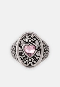 Anillo de tono plateado con forma ovalada y grabados florales. En el centro se encuentra una piedra preciosa rosa en forma de corazón, que realza su intrincado diseño.