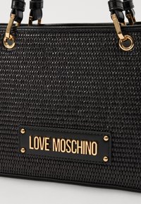 Bolsa tecida preta com hardware em tom dourado, um detalhe em pele lisa e o logótipo "LOVE MOSCHINO" em destaque.