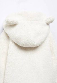 Vit plyschkappa med huva som har rundade öron, mjuk textur och en mysig, oversize design.