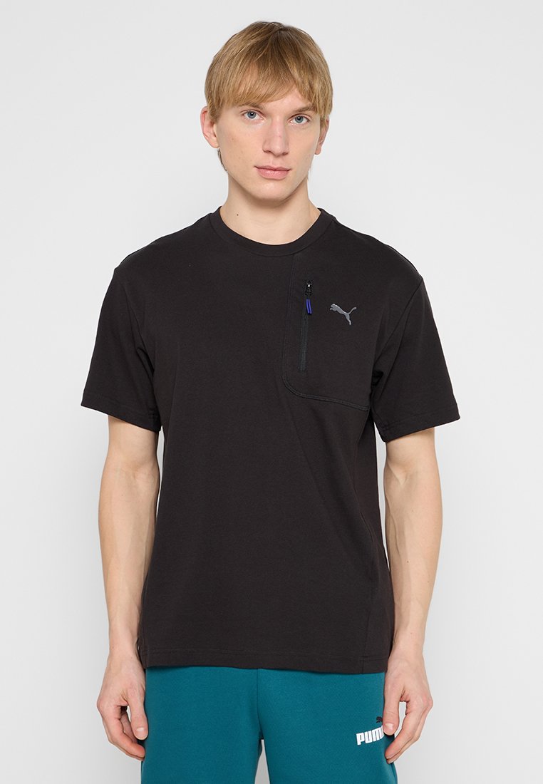 Camiseta negra de manga corta con cuello redondo, que presenta un bolsillo en el pecho con cremallera y un pequeño logo gris en el lado izquierdo. Tejido suave.