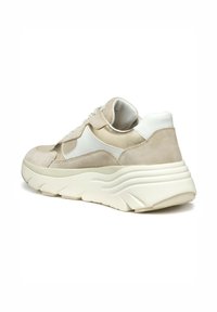Zapatillas beige y blancas con parte superior de gamuza y malla, suela de goma gruesa y ondulada, acentuadas con detalles dorados y cordones, cuello acolchado.