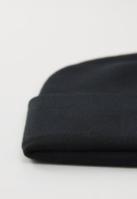 Zwarte gebreide beanie muts, omgevouwen aan de rand, geplaatst op een witte ondergrond, die de ribbelstructuur en de gladde stof toont.