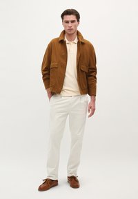 Brun corduroy jakke med to forlommer, beige polo skjorte, hvide bukser og brune snøresko, sat mod en neutral baggrund.