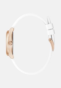 Kitsas roosa kuldne kellakorpus valge nahkrihma ja roosa kuldse pandlaga, nähtud küljelt helesinisel taustal.