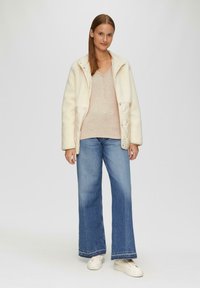 Weiße gesteppte Jacke, hellrosa strukturiertes Sweatshirt und weite blaue Jeans mit ausgefranstem Saum, kombiniert mit weißen Sneakers. Modell steht gerade.