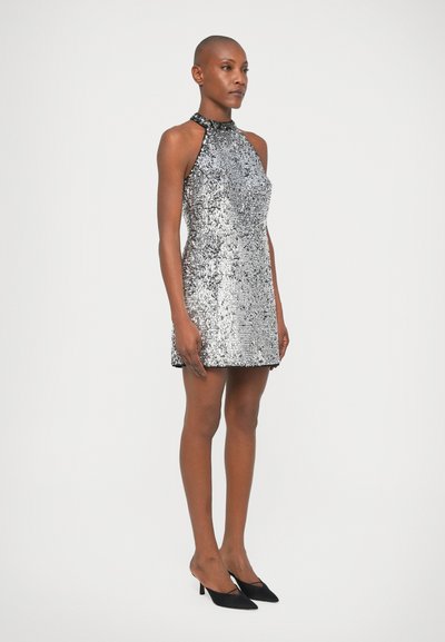 Silberner Pailletten-Minikleid mit Neckholder-Design, das eine figurbetonte Silhouette und schwarze Akzente am Halsauschnitt aufweist. Schwarze High Heels.