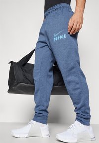 Blå melerede sweatpants med elastisk talje, med et hvidt Nike logo på låret og ribbede afslutninger, parret med hvide sneakers.