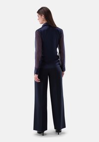 Navy-Bluse mit transparenten Ärmeln und klassischem Kragen, kombiniert mit weit geschnittenen navyblauen Hosen. Merkmale sind Knöpfe und eine fließende Silhouette.