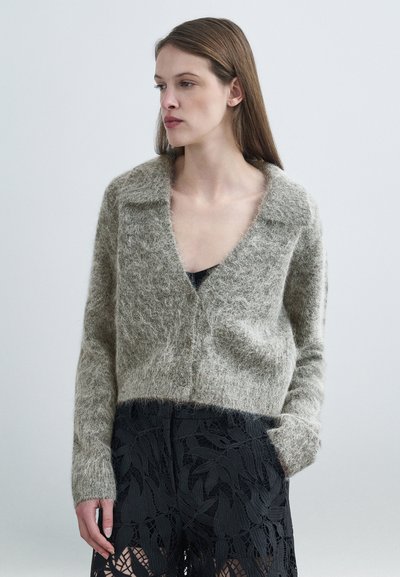 Light gray, fuzzy cardigan with a deep V-neck, button closure, and long sleeves. Paired with black lace shorts featuring leaf patterns.