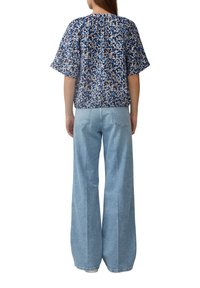 Kortebloesem top in blauw met geometrische patronen, gecombineerd met hoge taille lichtblauwe wijde jeans, gezien van achteren.