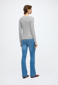 Sivý rebrovaný top s dlhými rukávmi a vlnitým lemom, nosený s modrými zvonovými džínami. Džínsy majú mierne vyblednutú textúru a sú dĺžky po členky.