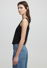 Top senza maniche nero in una vestibilità rilassata, realizzato in tessuto testurizzato, abbinato a jeans in denim blu a vita alta con taglio classico.