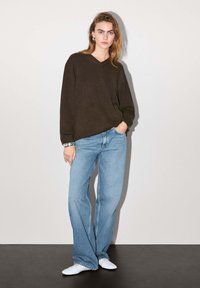 Brun V-ringad stickad tröja i kombination med ljusblå vida jeans och vita skor, som visar en avslappnad passform och mjuk textur.