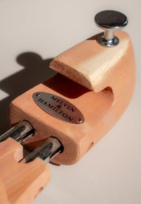 Holzschuhdehner in natürlicher Ausführung mit Metallbeschlägen, ausgestattet mit einer abgerundeten Vorderseite und einer Metallplakette, die mit "MELVIN & HAMILTON" graviert ist.