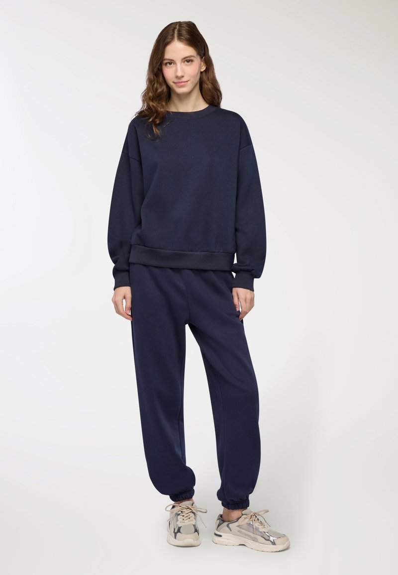Felpa blu navy con vestibilità rilassata e polsini a coste, abbinata a pantaloni jogger coordinati con caviglie arricciate.