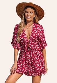 Salopette floreale rossa con maniche a volant e vita con cintura, realizzata in tessuto leggero. Presenta motivi floreali bianchi e una vestibilità ampia.