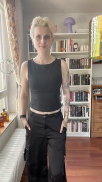 Zwarte cropped tanktop met een ronde halslijn, gecombineerd met een ruime zwarte cargobroek met zakken. Achtergrond van lichthouten vloer.