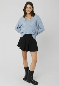 Un pull bleu clair à col en V en matériau doux, associé à une mini-jupe plissée noire. Des bottes noires montant jusqu'au genou avec des semelles épaisses.