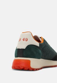 Sneakers in suede verde e tessuto testurizzato con accenti arancioni, tallone bianco e dettaglio rosso "1949" sul retro. Suola in gomma solid a.