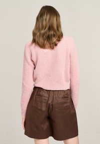 Rosa gestrickter Pullover mit lockerer Passform und geripptem Saum, kombiniert mit braunen, satinartigen High-Waist-Shorts mit seitlichen Taschen.
