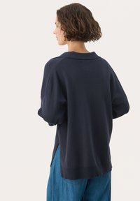 Donkerblauwe oversized trui met kraag, ribgebreide zomen en zijspleten. Zachte textuur, casual pasvorm en ontspannen mouwen.
