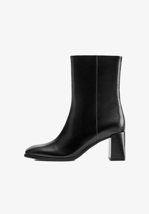 Botte noire en cuir mi-mollet avec bout pointu et talon bloc sur fond blanc, vue de côté.