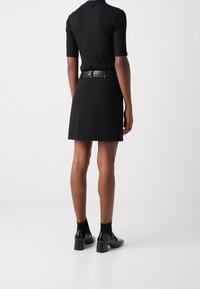 Persona che indossa un top nero a maniche corte infilato in una mini gonna nera con una cintura nera, abbinato a calze nere e scarpe con tacco bloccato lucide nere.