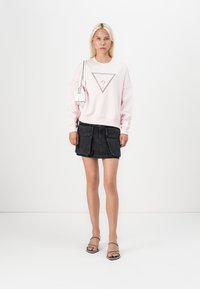 Pink sweatshirt with triangle graphic, paired with a black denim skirt featuring dual front pockets. Model wears black sandals and holds a white bag.