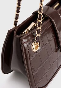 Borsa a tracolla in pelle marrone scuro con motivo coccodrillo, dotata di tracolla in catena dorata e chiusura a zip, mostrata in primo piano.