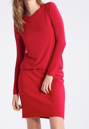 Abito rosso a maniche lunghe con scollatura arrotondata. Tessuto morbido e aderente; lunghezza al ginocchio. Parte superiore a strati sopra una gonna attillata. Design minimalista.