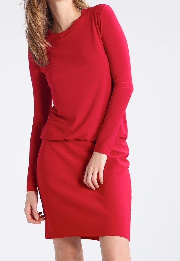 Robe rouge à manches longues avec un col rond. Tissu lisse et ajusté ; longueur au genou. Haut superposé sur une jupe près du corps. Design minimaliste.