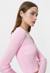 Cardigan a coste rosa con scollo a V, maniche lunghe e chiusura anteriore con bottoni. Presenta una vestibilità aderente e una texture liscia.