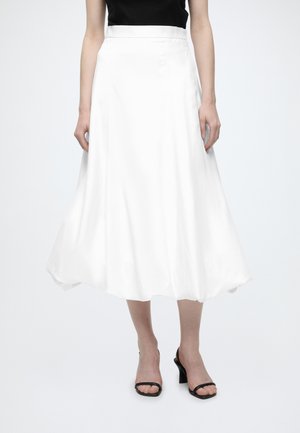 Femme portant une jupe midi blanche taille haute avec des sandales noires à talons ouvertes et un top noir sans manches.
