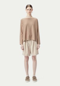 Brun långärmad topp tillsammans med beige shorts, med en avslappnad passform. Bruna sneakers med ljusa sulor fulländar outfiten.