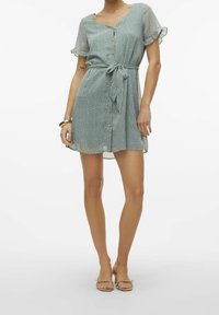 Grünes Polka-Dot-Kleid mit kurzen Ärmeln, Knopfleiste und Bindegürtel. Weicher Stoff, knielang mit lässiger Passform und Rüschensäumen.